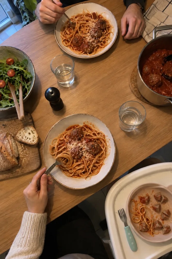 De gezinstafel om zes uur: balletjes in tomatensaus voor de volwassenen en in vieren gesneden op het blad van de kinderstoel